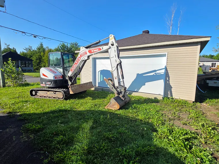 Avant : la pelouse et les mauvaises herbes jusqu'à la porte du garage, la mini-excavatrice de l'équipe arrivée sur place